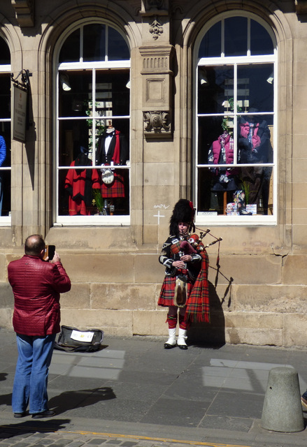 A bagpiper in full Highland dress performing for visitors on Edinburgh's Royal Mile