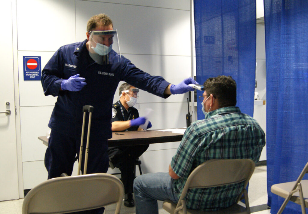Airport health worker checking an arriving passenger's temperature at a screening desk