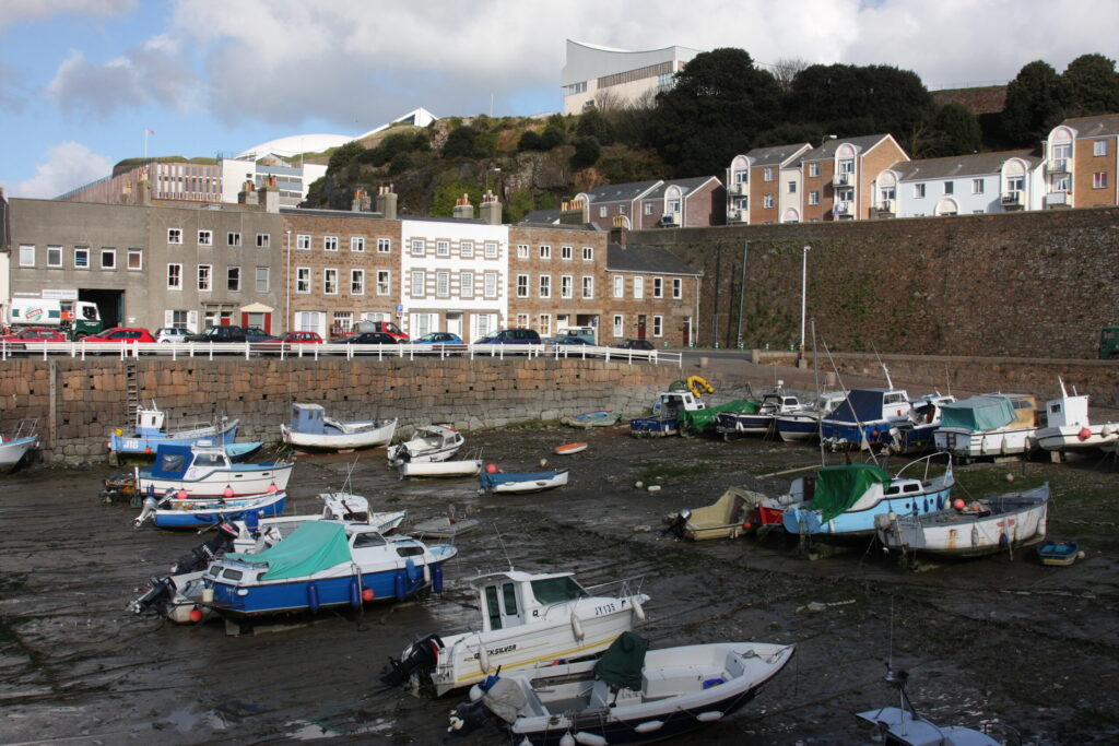 Boats moored in St Helier harbour marina, Jersey, at low tide with townhouses behind