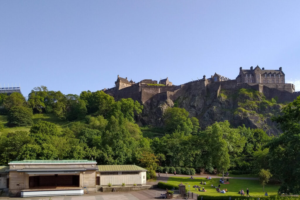 Edinburgh Castle on its crag above Princes Street Gardens with visitors on the grass