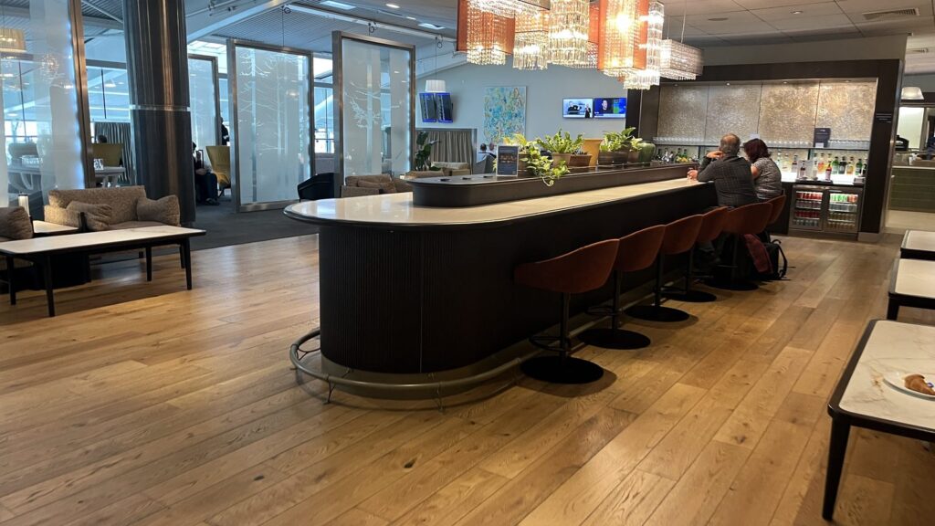 Oval island bar at the BA Galleries Club T5B Heathrow lounge, with crystal chandeliers and rust velvet chairs