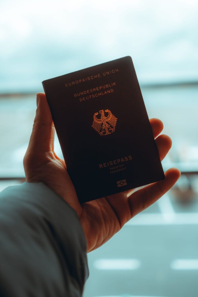 Person holding German EU passport at airport departure gate with aircraft visible
