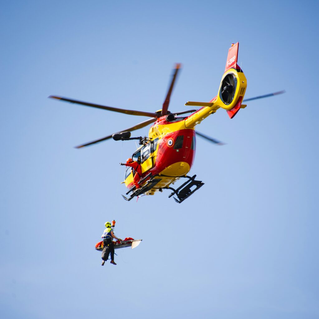 Red and yellow search and rescue helicopter flying in French Alps blue sky