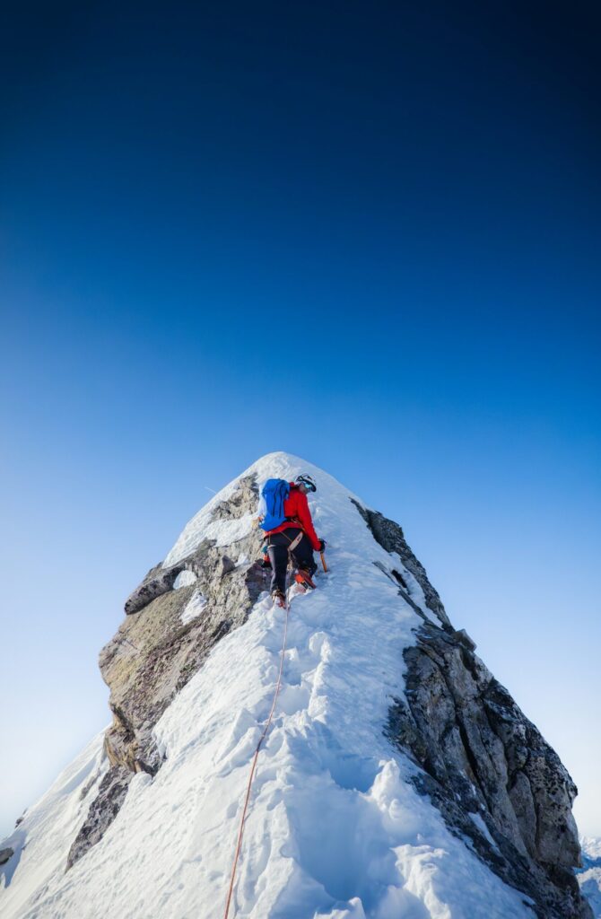 Solo mountaineer ascending steep snow-covered mountain face in Austria blue sky