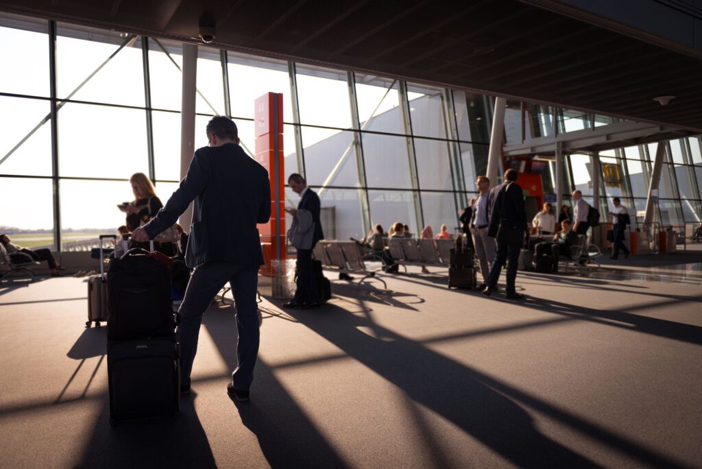 Traveler pulling rolling suitcase in modern airport departure lounge at sunset