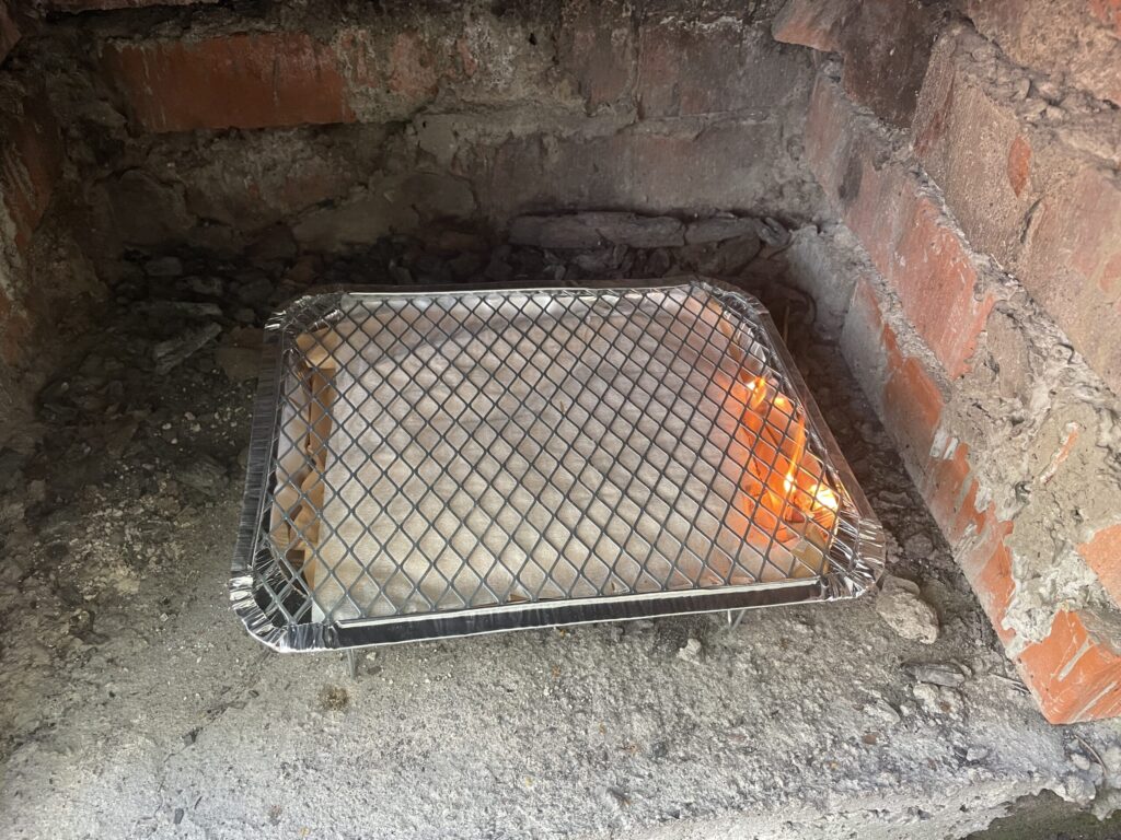 A lit disposable foil barbecue with flames visible under the grill