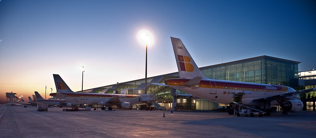 Aircraft on stand at Barcelona El Prat Terminal 1 at dusk with ground handling equipment