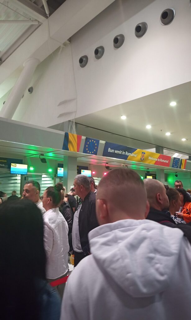 Crowded passport control queue under an EU flag and a Welcome to Romania sign at an airport