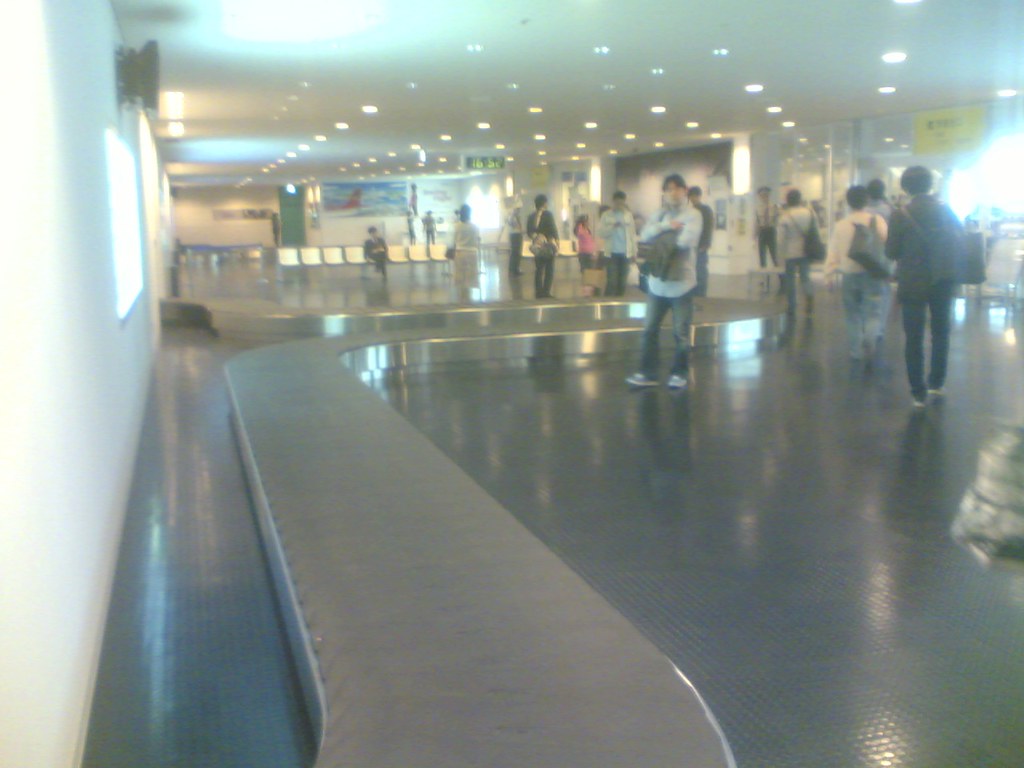 Empty baggage reclaim carousel with passengers waiting in an airport arrivals hall