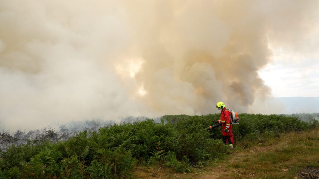 Firefighter using a blower against burning bracken on a Welsh hillside near Blaenavon