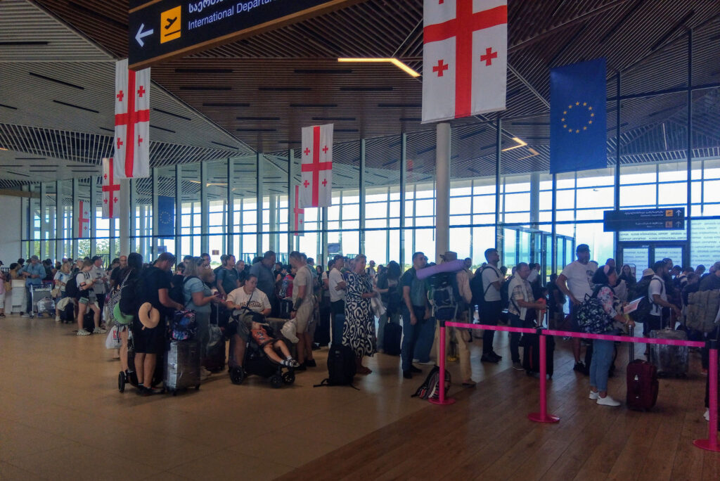 Long passenger queue at international departures under an EU flag at an airport terminal