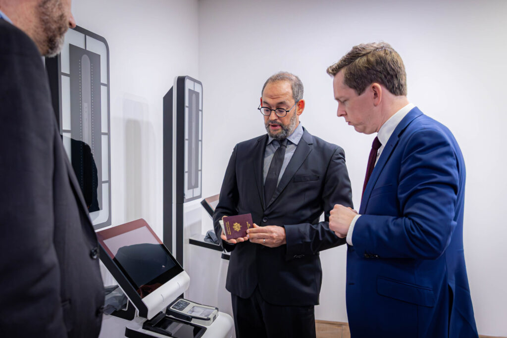 Officials inspecting a passport beside EES self-service kiosks at St Pancras International