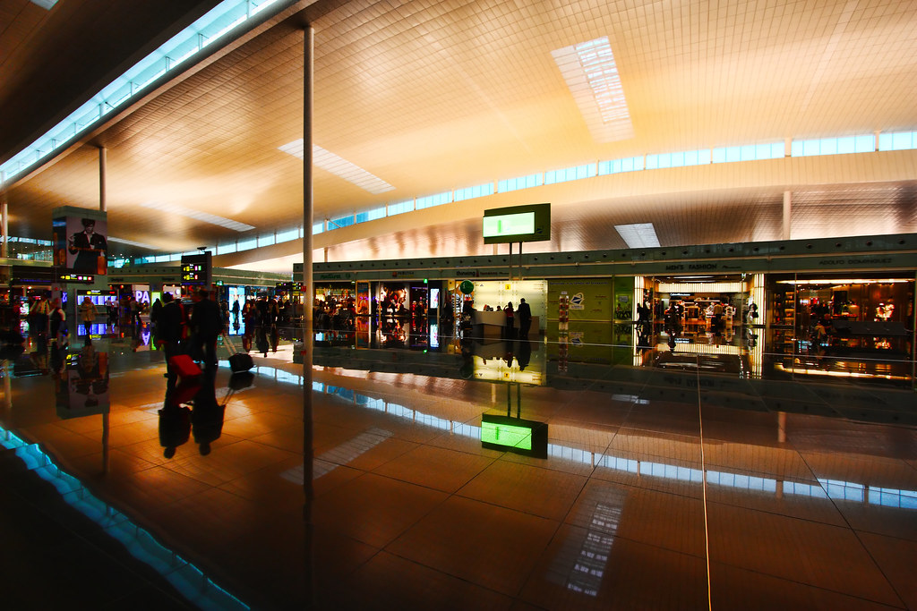Passenger wheeling a suitcase through the Terminal 1 concourse at Barcelona El Prat airport