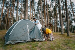 Family pitching a Trail Outdoor Leisure tent at a campsite with camping furniture set up nearby